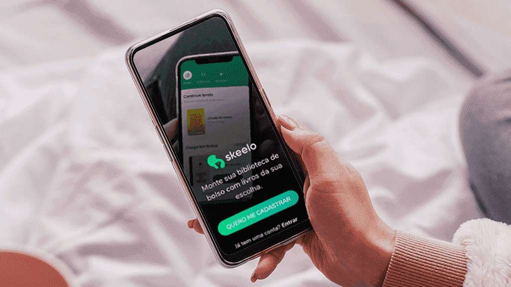 Uma mão segurando um celular. Na tela, o acesso principal ao aplicativo do Skeelo.